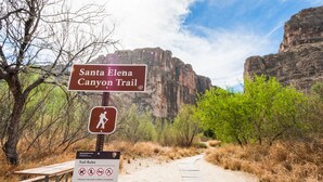 Un letrero de indicaciones para el sendero Cañón Santa Elena, con una mesa de picnic y un cartel que detalla las normas del sendero.