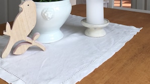 Un pot en céramique blanche orné de fleurs roses et d’une décoration en forme d’oiseau en bois, posé sur une table.