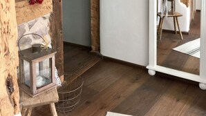 Une pièce avec des poutres apparentes, une cheminée en pierre, un grand miroir blanc et une petite table en bois sur laquelle est posée une lanterne.