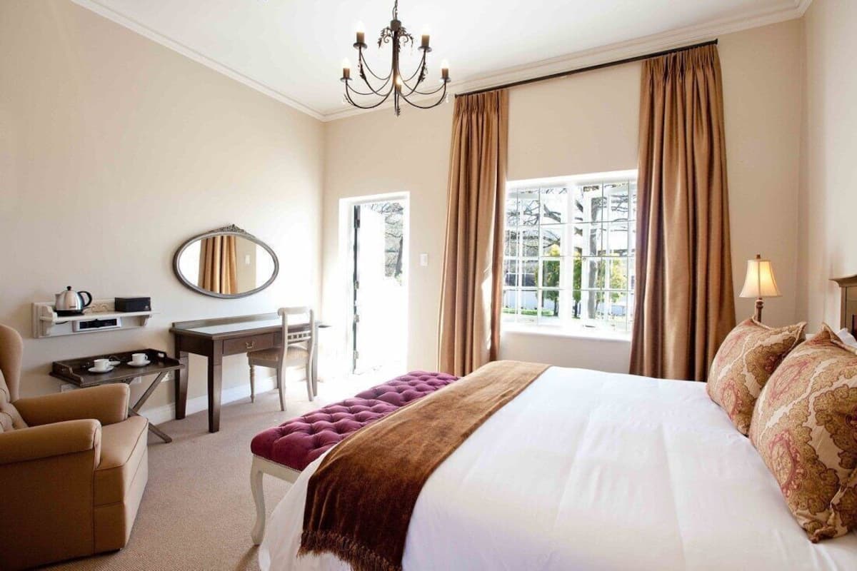 A hotel room with a bed, a desk, a chair, a mirror, and a window with curtains.