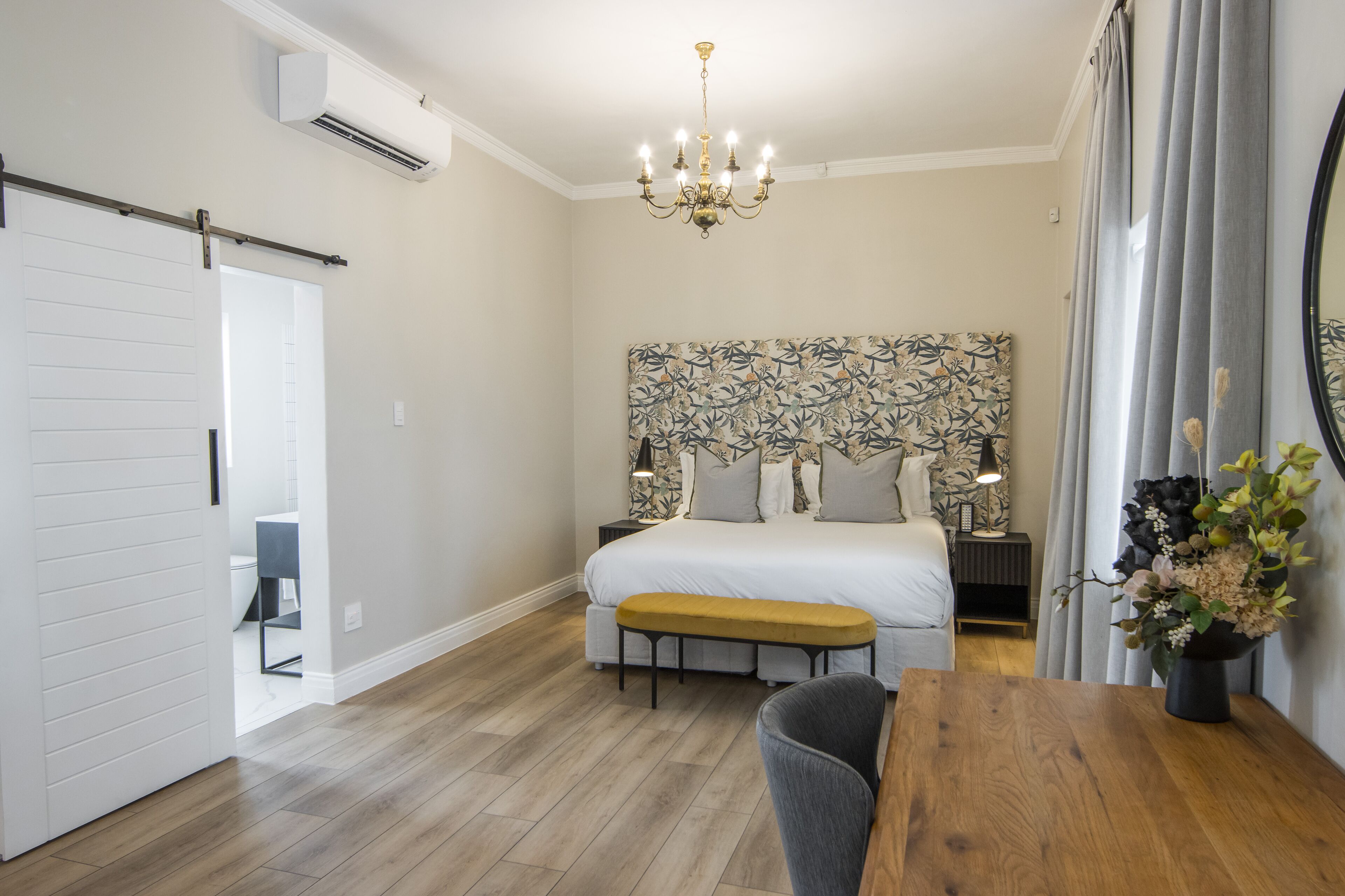 A bedroom with a bed, bedside tables, a bench, a wooden table, and a chandelier.