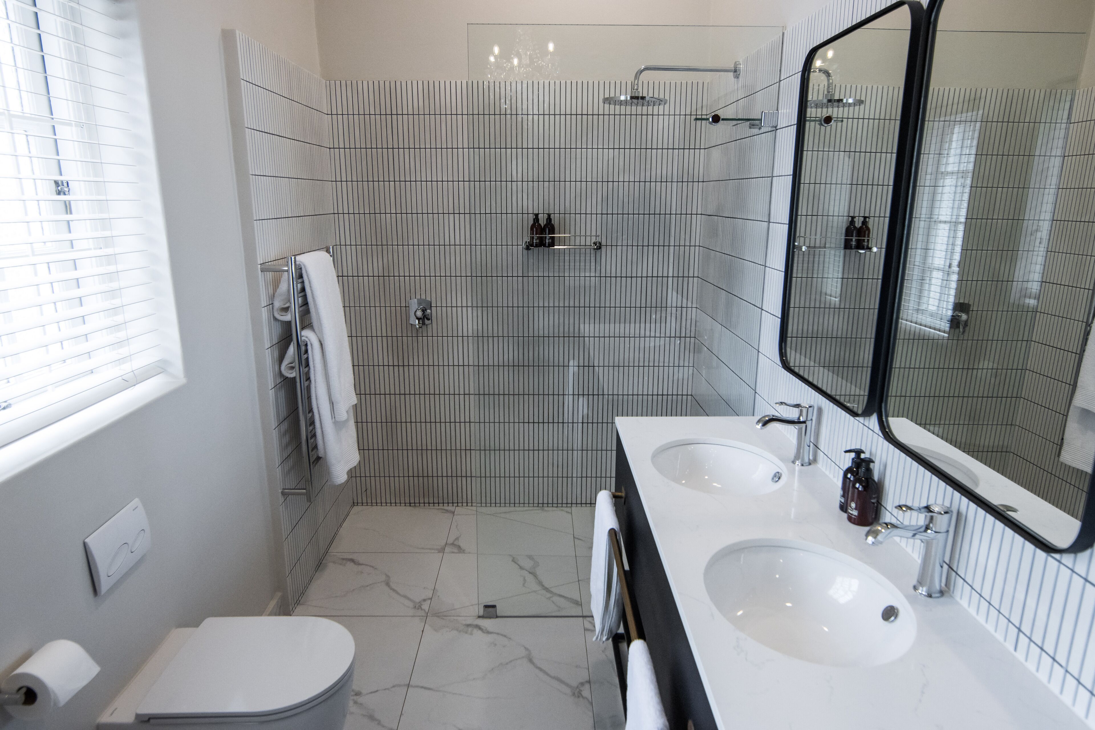 Uma casa de banho moderna com duas pias, sanita, chuveiro e um espelho grande.