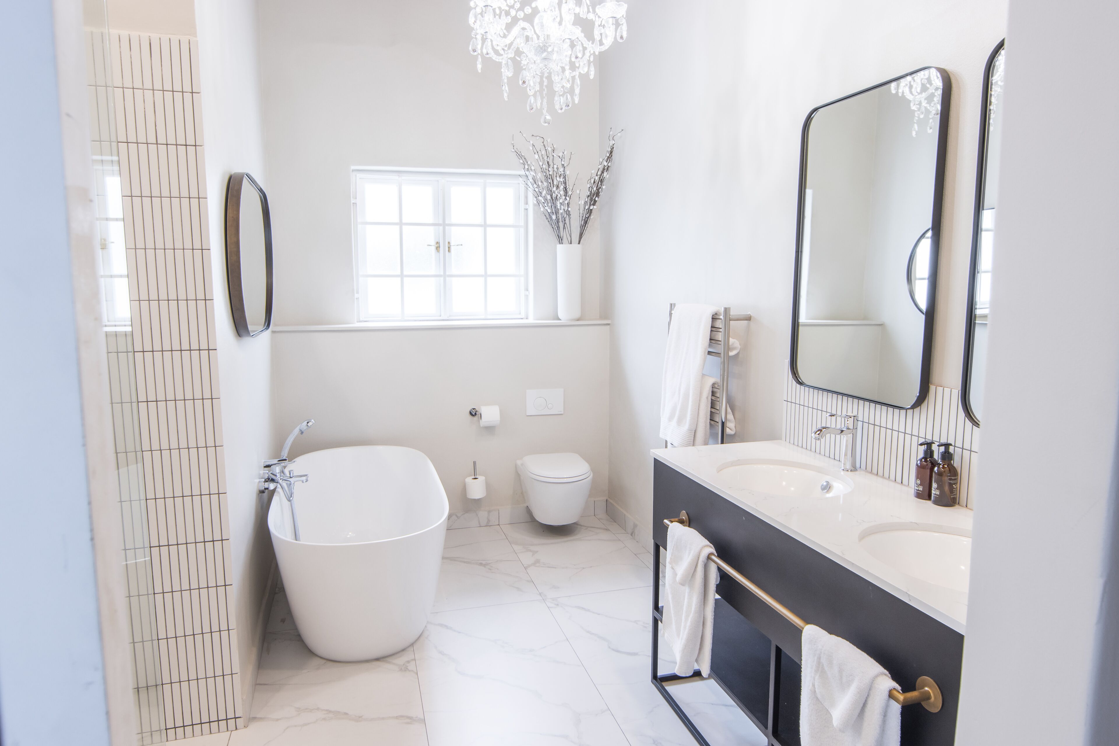 A modern bathroom with a freestanding bathtub, a large mirror, and a vanity with a sink and towel rack.
