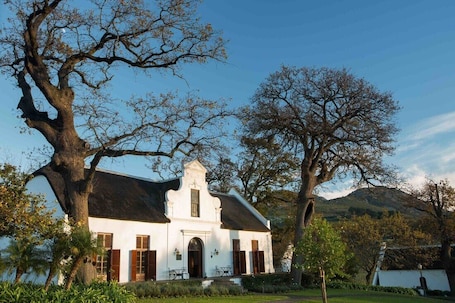 A white building with a steep roof, surrounded by trees and a mountain in the background.