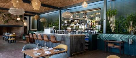 Un área de bar moderna con una barra alta, asientos con taburetes e iluminación colgante.