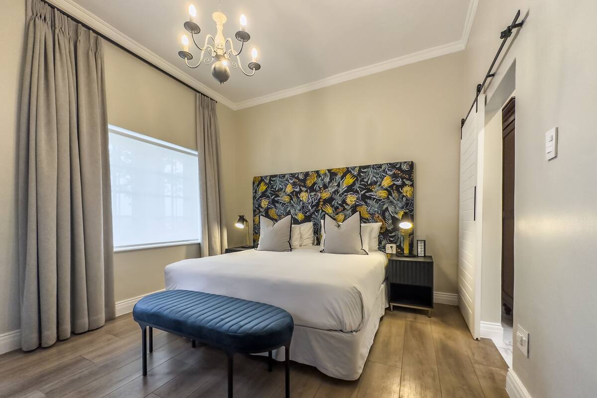 A bedroom with a large bed, a bench, a chandelier, and a floral headboard.