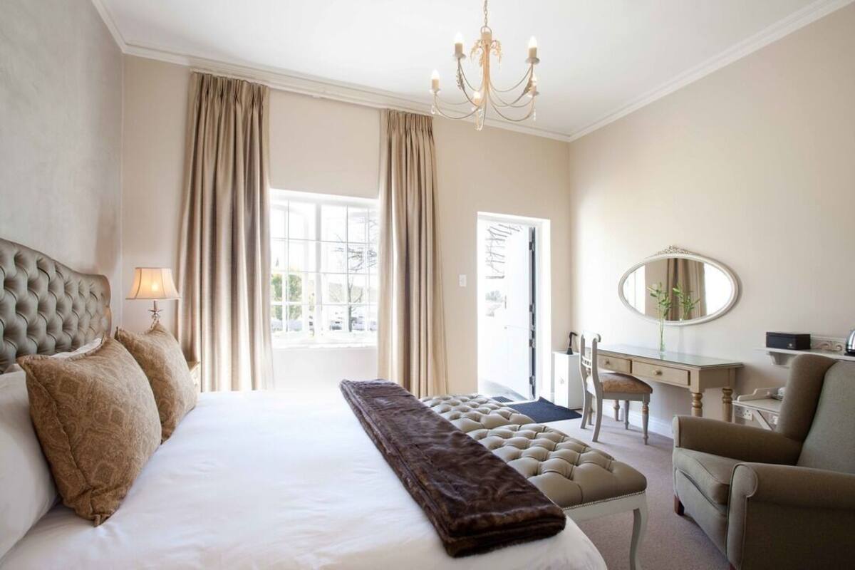 A hotel room with a large bed, a desk, a chair, a mirror, and a chandelier.