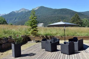 Una terraza con mobiliario exterior y un gran paraguas, con vistas a un paisaje montañoso.
