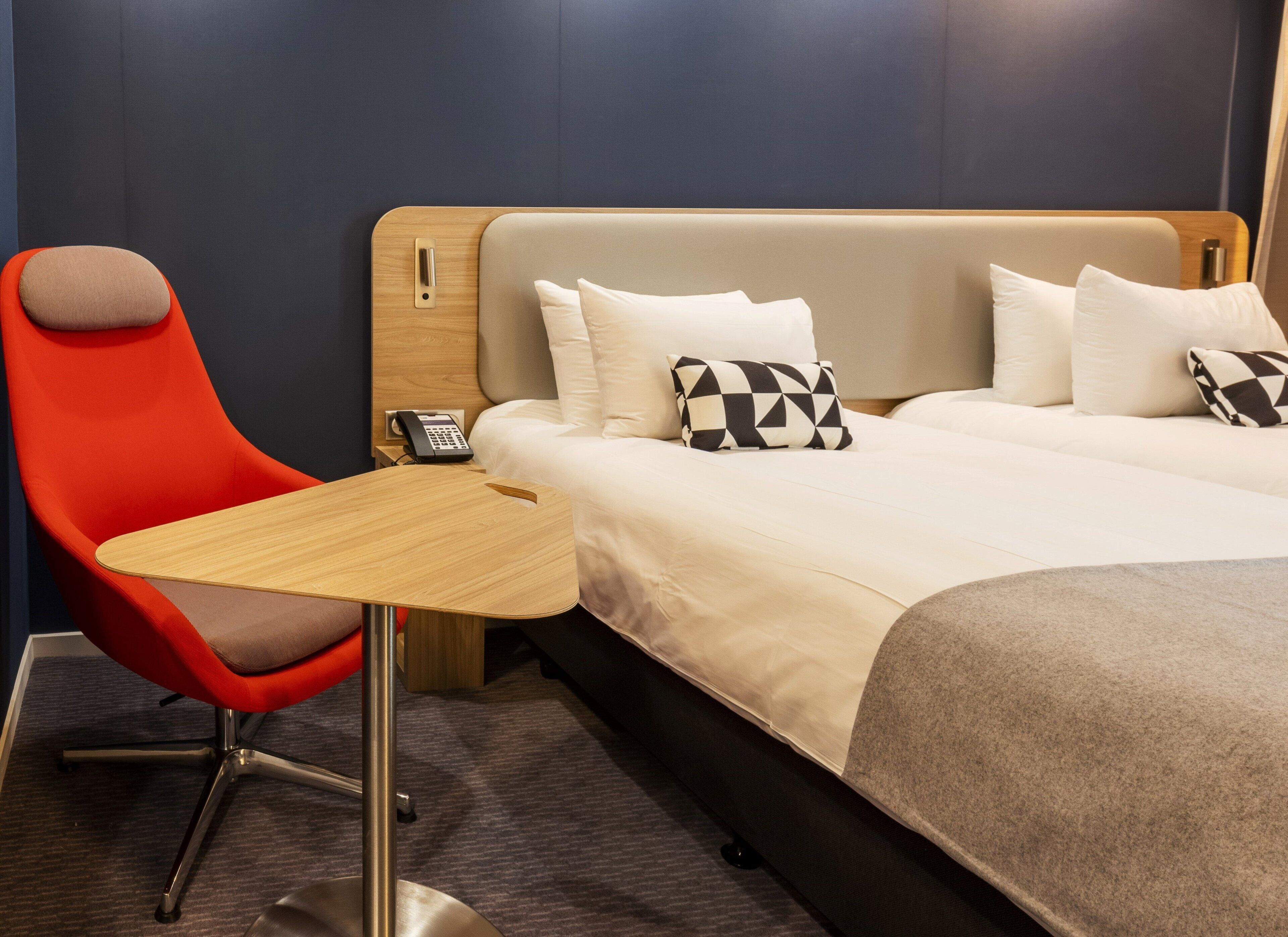 Hotellihuone, jossa on sänky, työpöytä ja punainen tuoli.