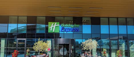 A Holiday Inn Express hotel with a glass facade, outdoor seating area, and potted plants.