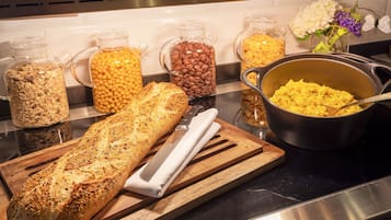 Una encimera de cocina con una hogaza de pan, tarros de avena y granos de café, y una cazuela de huevos revueltos.