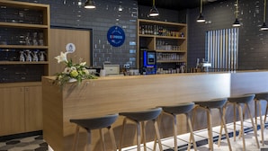 A modern bar area with a wooden counter, bar stools, and a variety of glassware.