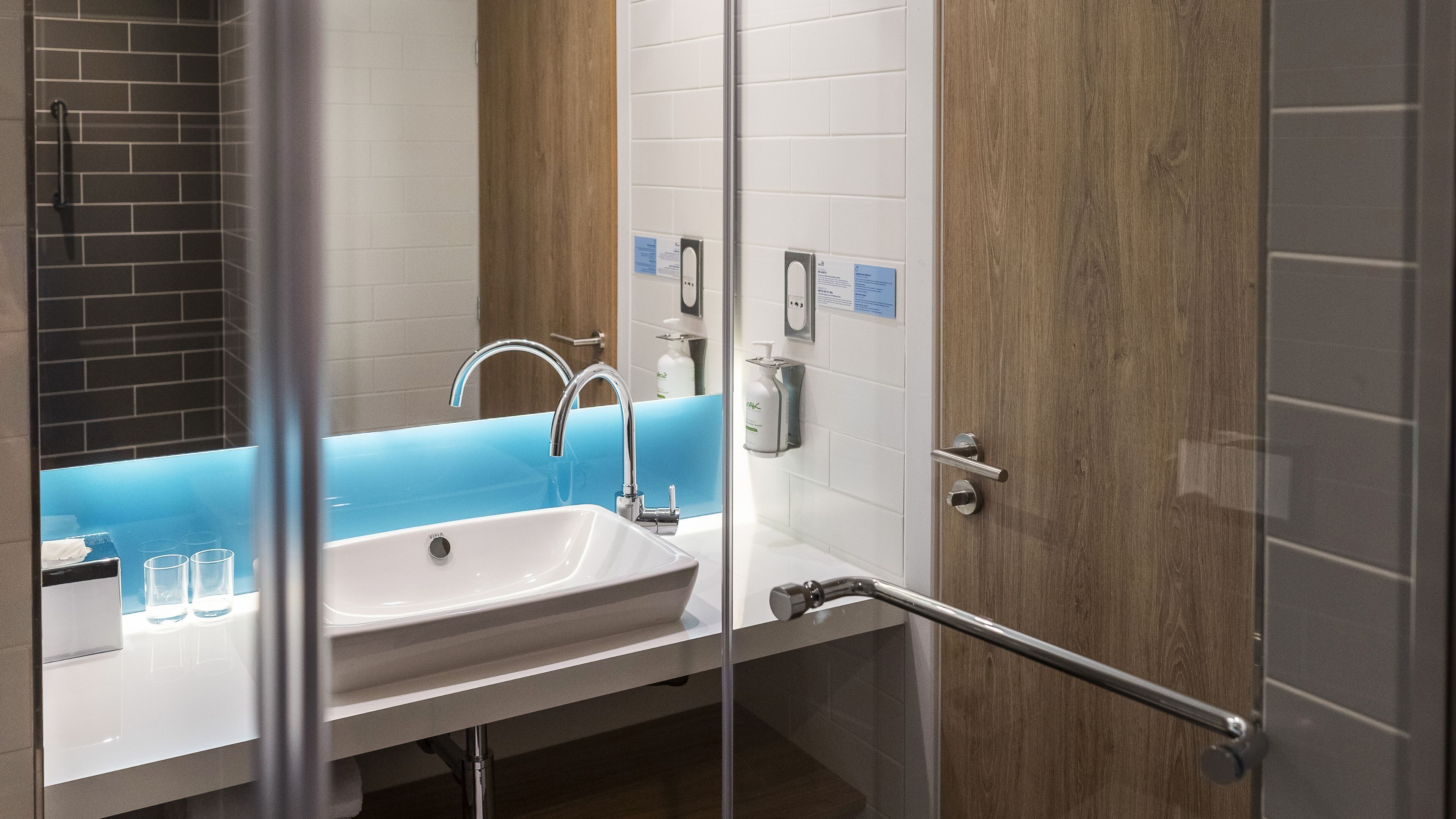 Un baño moderno con lavamanos blanco, encimera azul y cabina de ducha con mampara de vidrio.