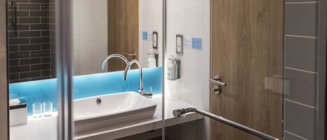 Un baño moderno con lavamanos blanco, encimera azul y cabina de ducha con mampara de vidrio.