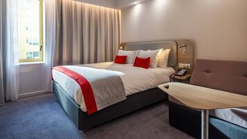 A hotel room with a bed, a bedside table, a chair, and a window with curtains.
