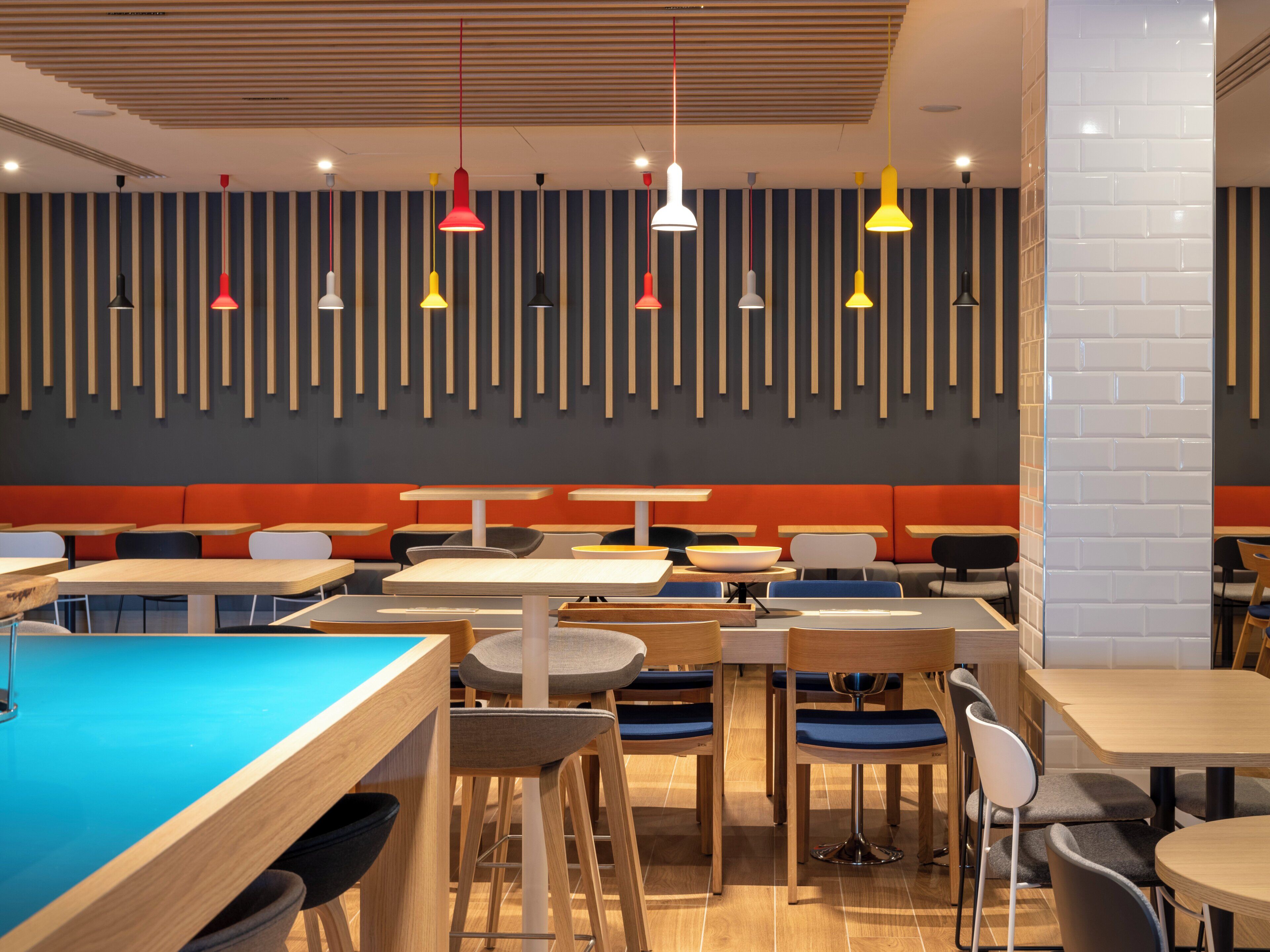 Un espace repas moderne doté de plusieurs tables et chaises, d’une table de billard et d’un mur avec des lambris en bois verticaux.