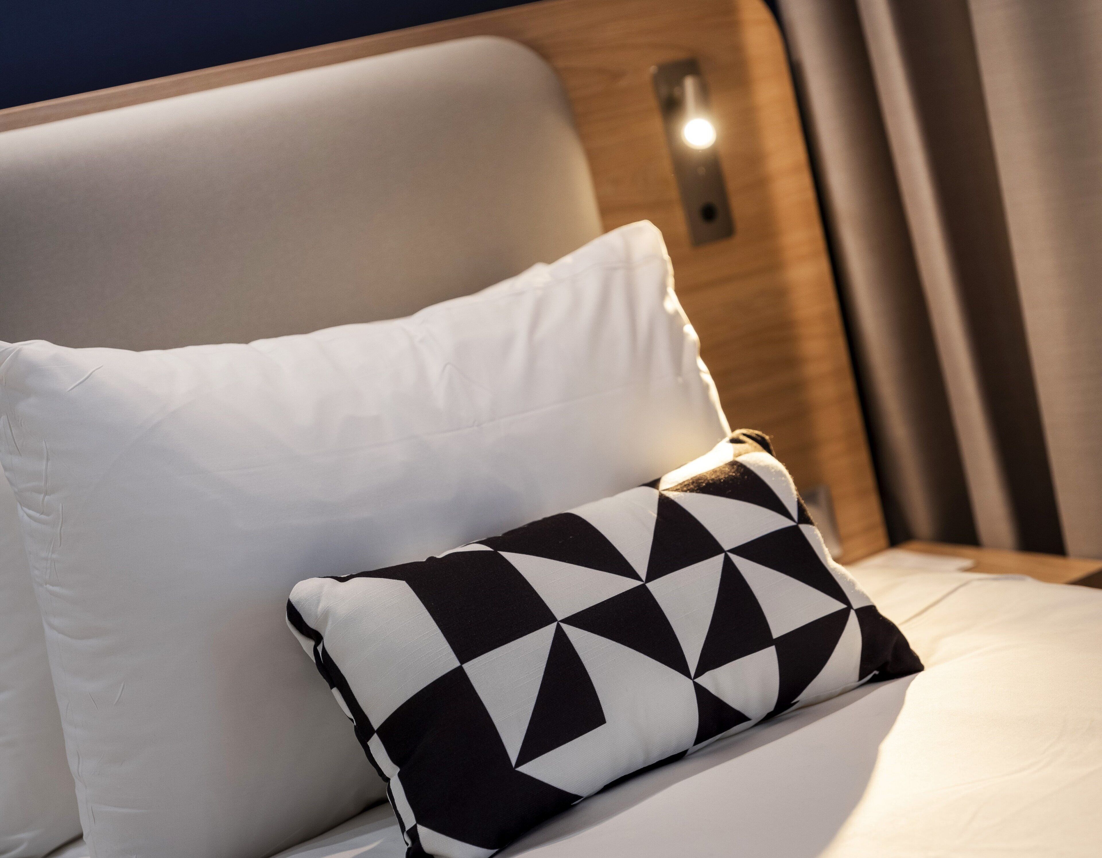 A bed with a white pillow and a black and white patterned pillow.