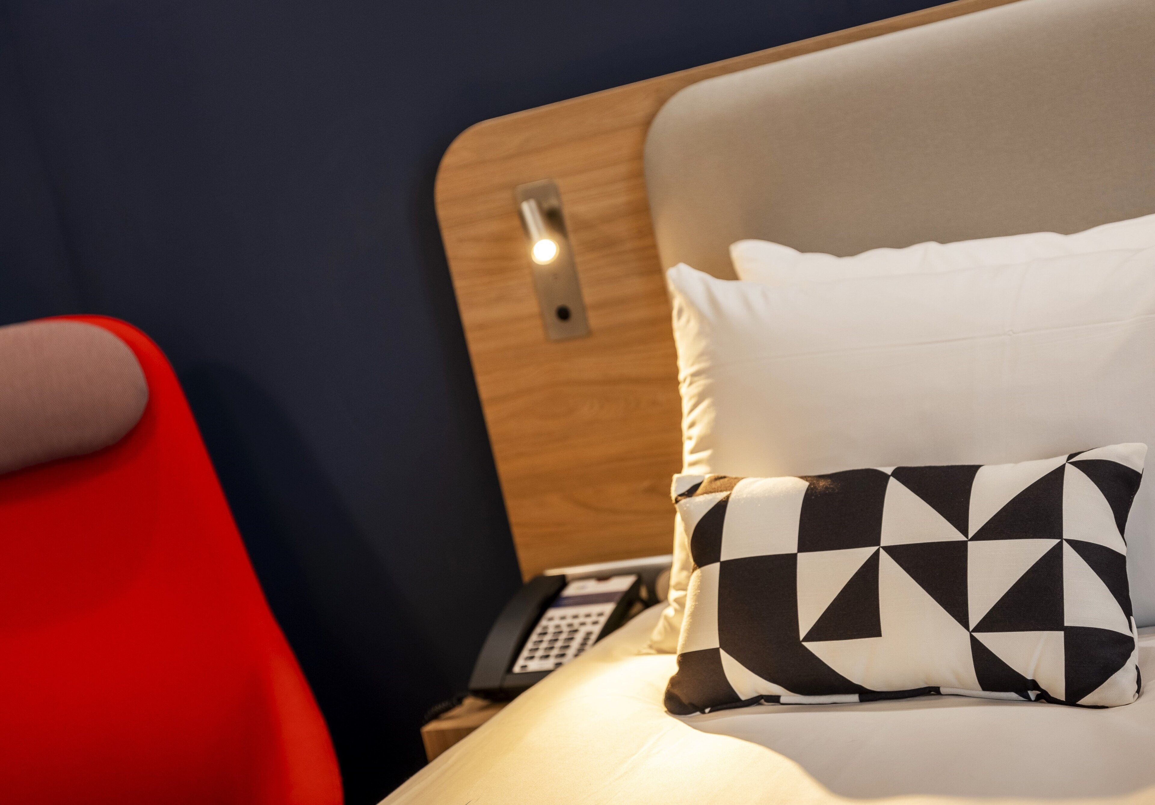 A hotel room with a bed, a red chair, and a bedside table with a telephone.