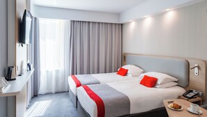 A hotel room with a bed, bedside table, and a TV mounted on the wall.