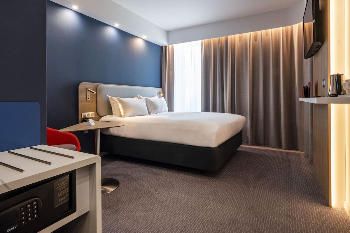 Ein modernes Hotelzimmer mit einem großen Bett, einem Schreibtisch und einem an der Wand montierten Fernseher.