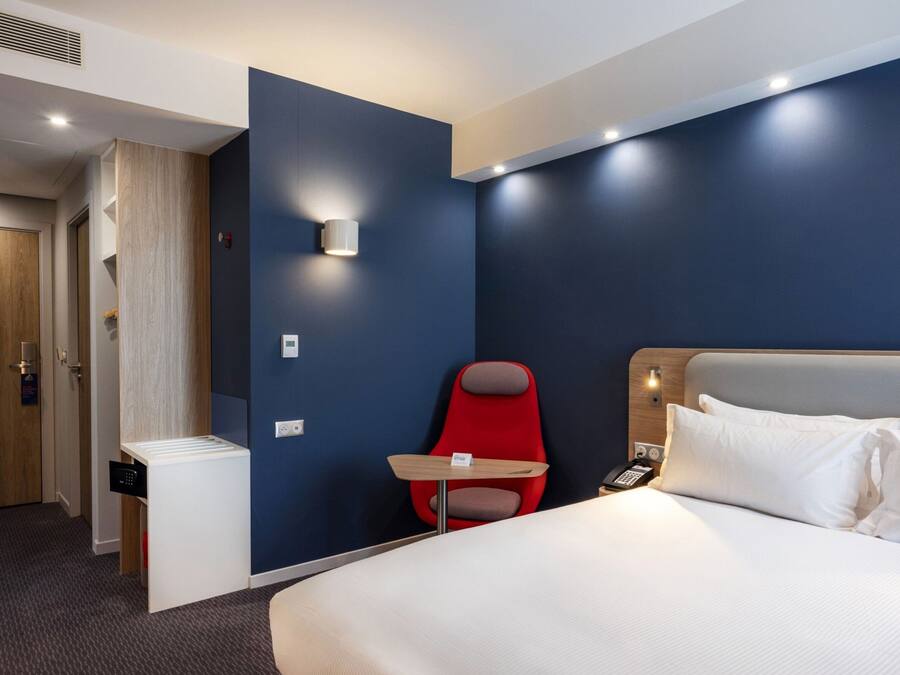 Une chambre d’hôtel avec un lit, une chaise rouge, une petite table et un téléphone fixé au mur.