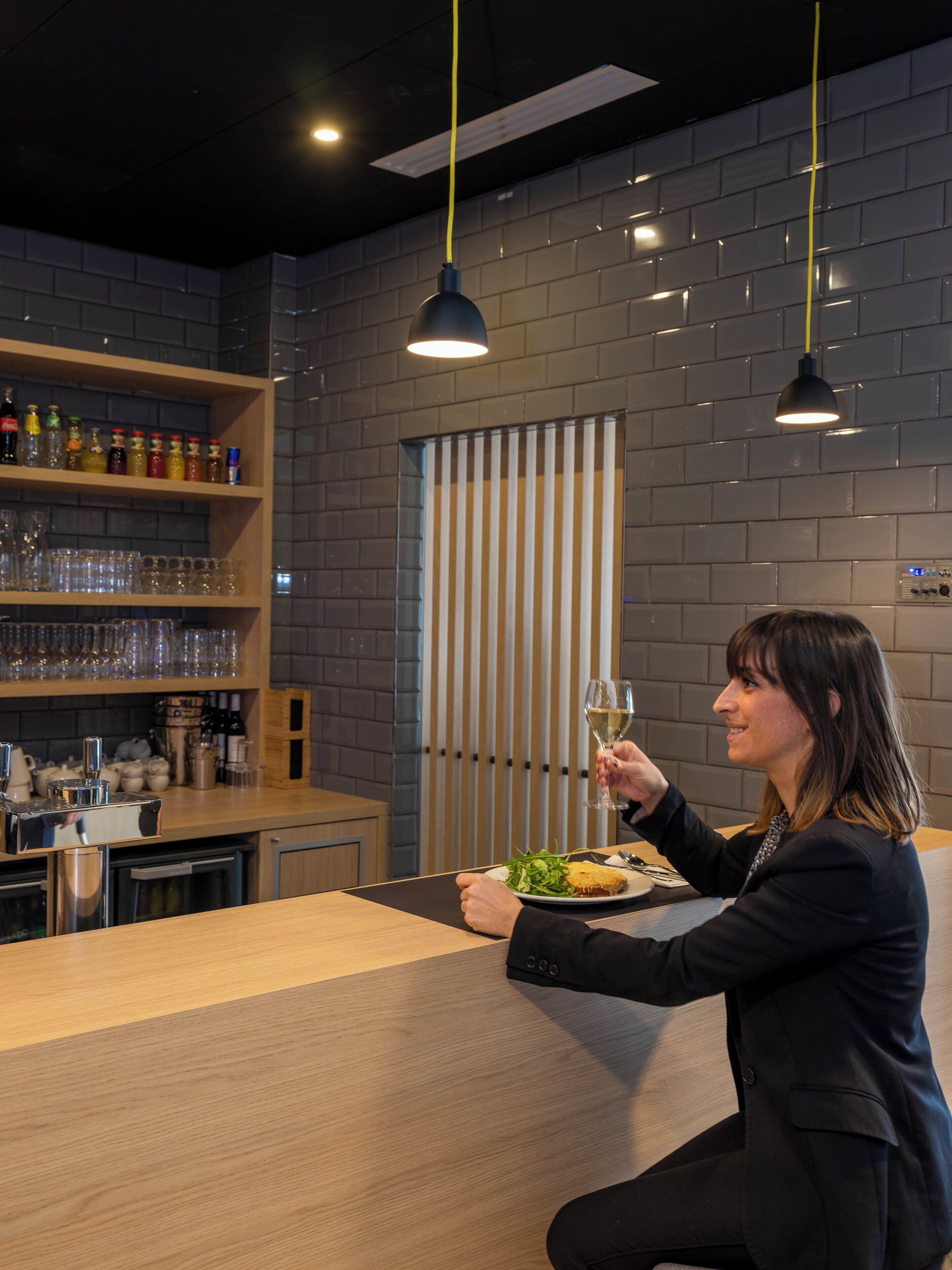 Een modern interieur met een bar, planken vol flessen en glazen, en een persoon die een glas vasthoudt.
