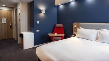 Une chambre d’hôtel avec un lit, une chaise rouge, une petite table, un téléphone et une lampe fixée au mur.