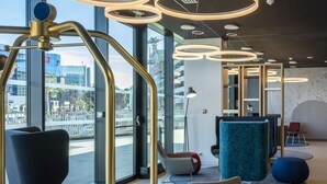 A modern interior with seating, a reception desk, and large windows offering city views.