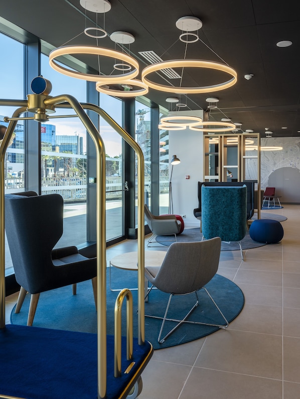 A modern interior with seating, a reception desk, and large windows offering city views.