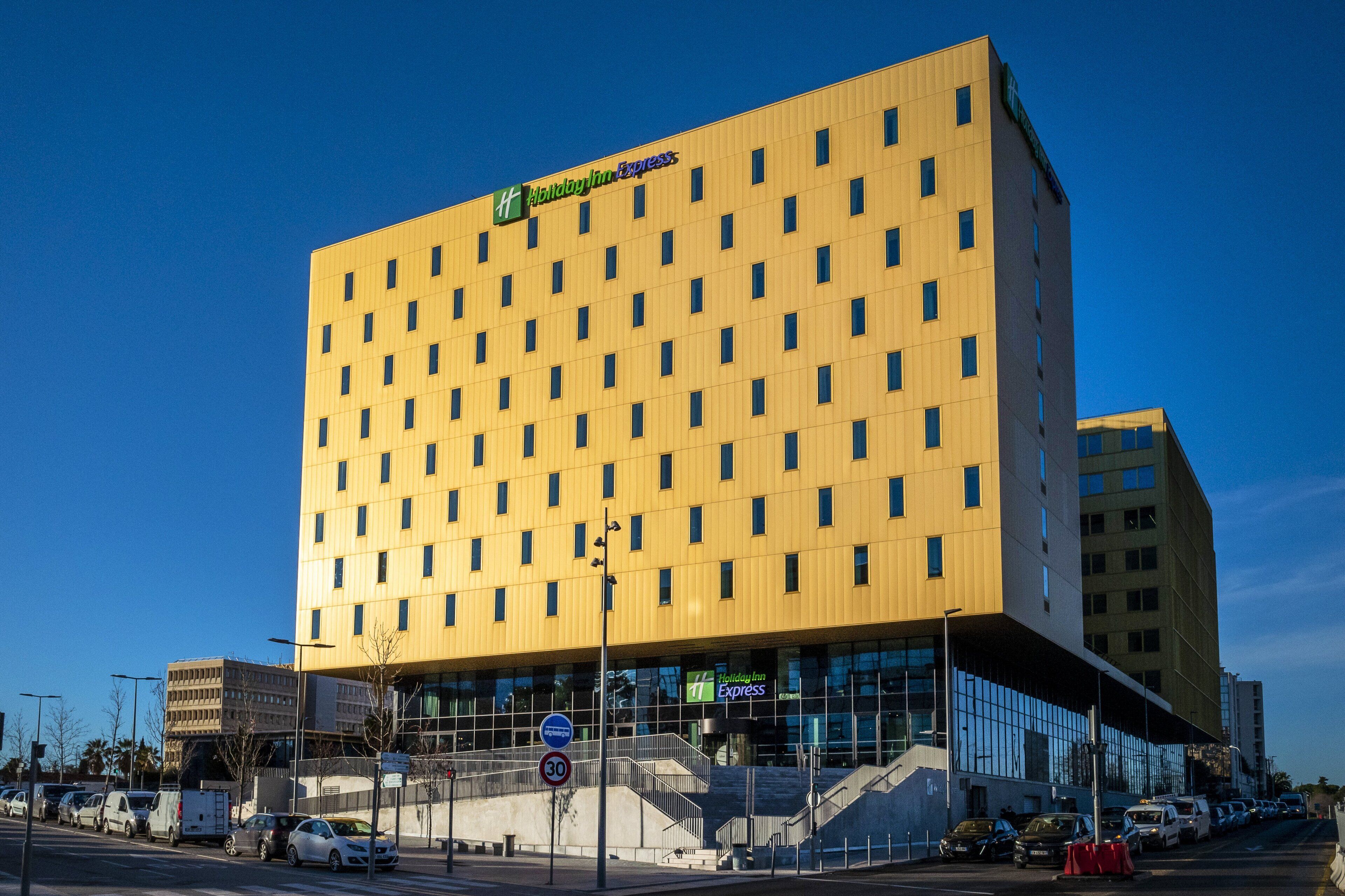 A modern Holiday Inn Express hotel with a yellow facade, large windows, and a visible entrance.
