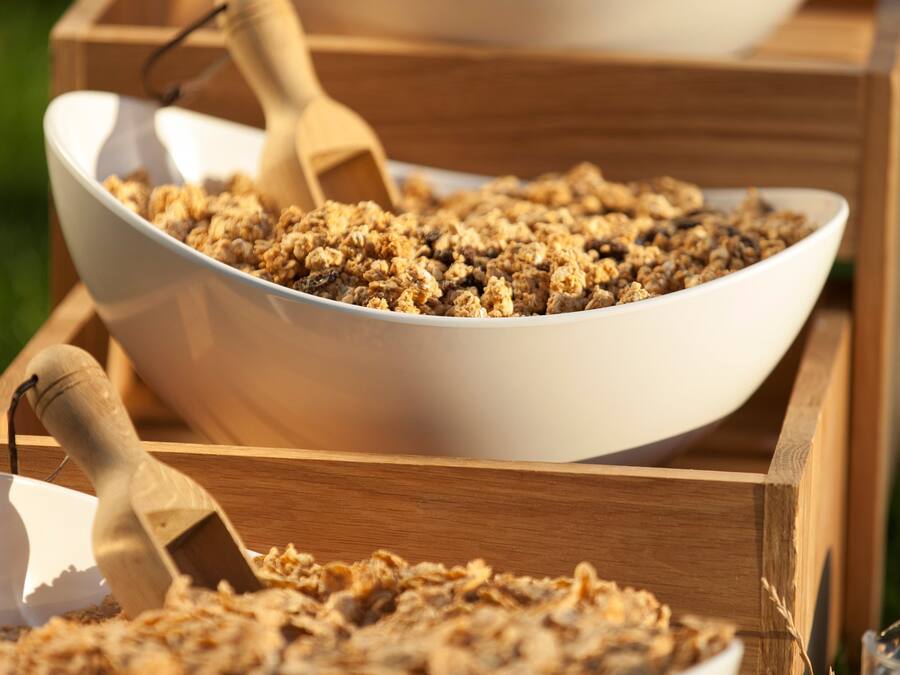 A wooden serving tray with a white bowl containing granola.