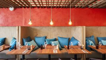 Un restaurante con mesas de madera, cojines azules y bombillas colgantes.