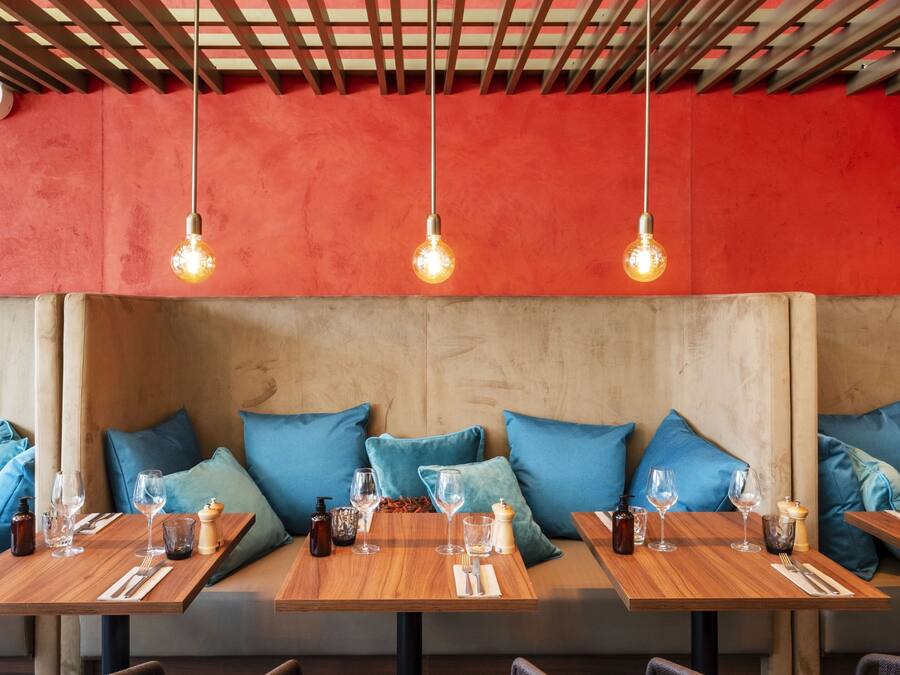 Un restaurante con mesas de madera, cojines azules y bombillas colgantes.
