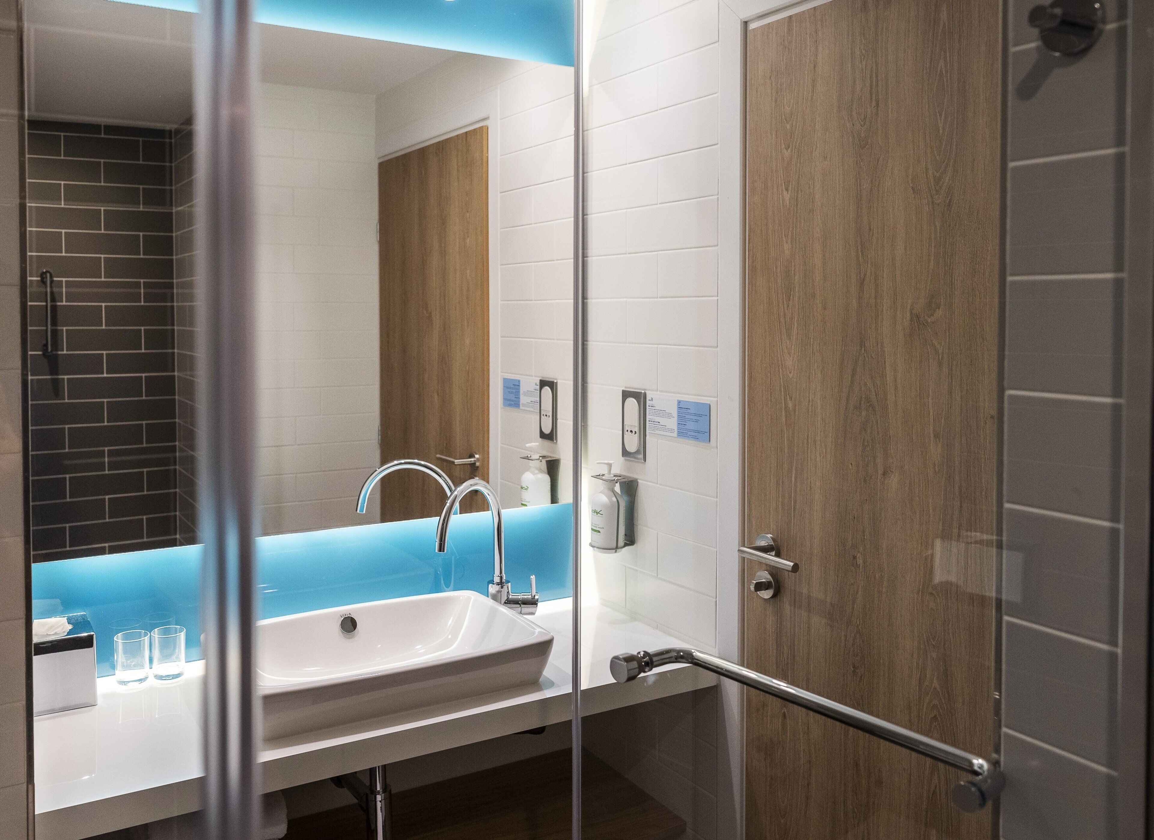 Un baño moderno con un lavamanos blanco, dos grifos y una puerta de madera.