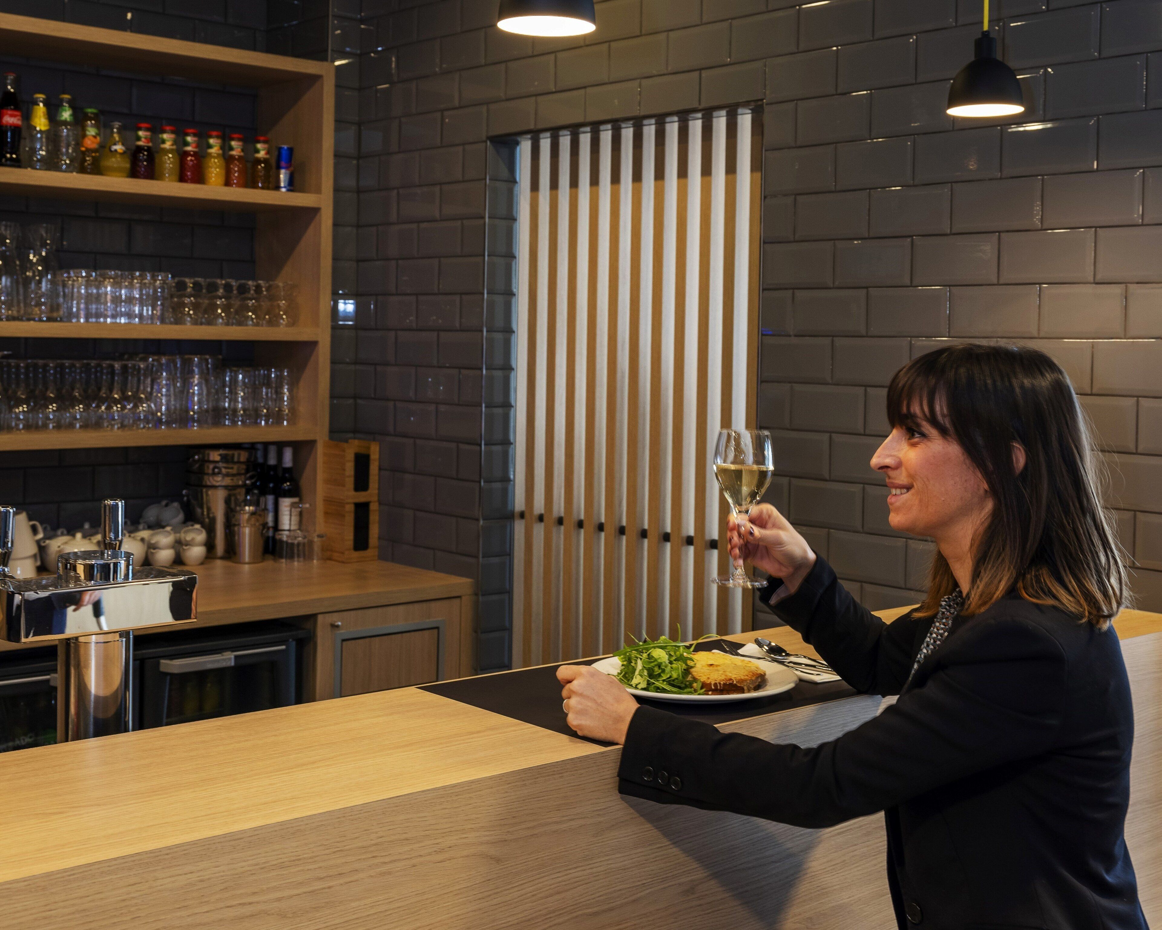 A person holding a wine glass at a bar with shelves of bottles and glasses.
