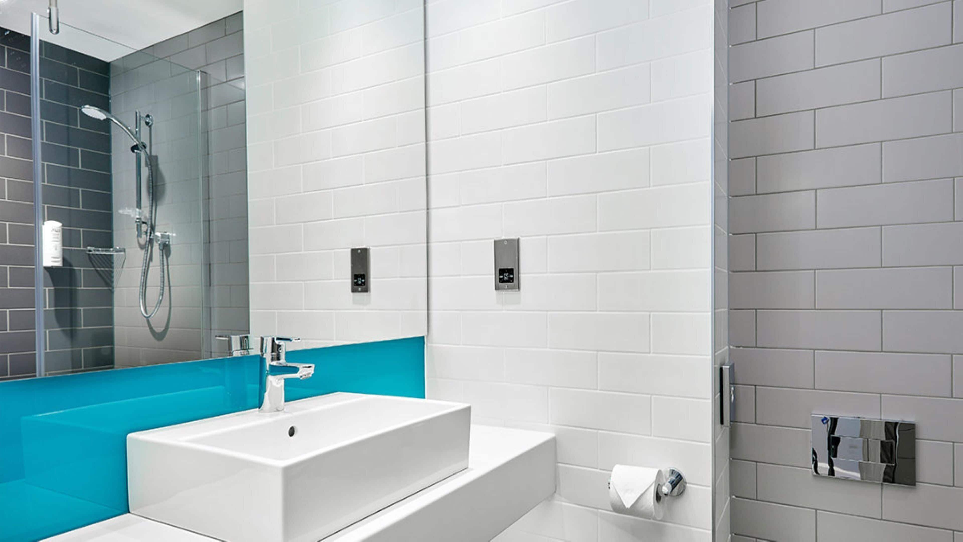 Une salle de bain moderne avec un lavabo blanc, une douche en verre et un mur d’accent bleu.