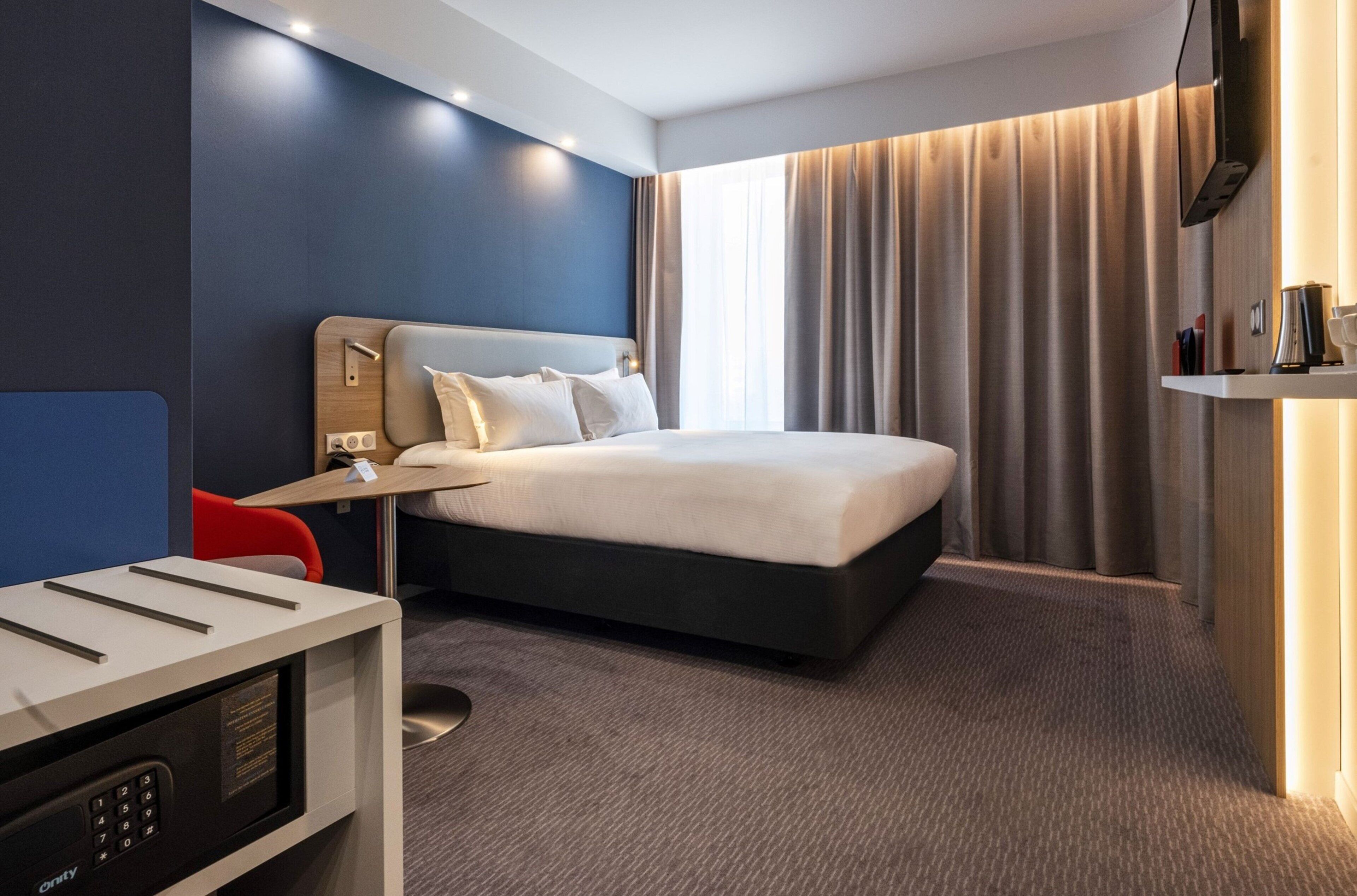 A modern hotel room with a large bed, a desk, a chair, and a television.