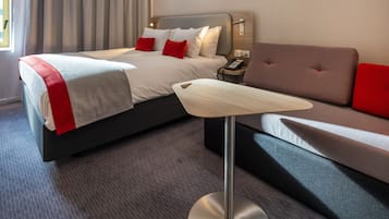 Ein modernes Hotelzimmer mit einem ordentlich bezogenen Bett, einem Sofa, einem Nachttisch mit Telefon und einer Lampe.