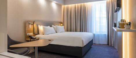 Een moderne hotelkamer met een groot bed, nachtkastje en bureau.