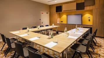 A conference room with a long table, chairs, water bottles, and a projector screen.