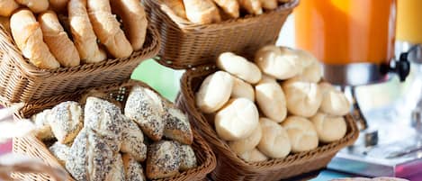 Cesti di pane e panini assortiti, una pagnotta e un bicchiere di succo d'arancia.