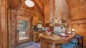 A wooden cabin interior with a kitchen area, a dining table, and blue stools. - Cute Studio Cabin! Views! Private. Hot Tub. Relax! (Sevierville)