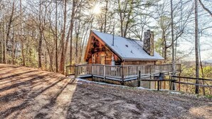 A cabin with a wooden exterior, a balcony, and a metal railing. - Cute Studio Cabin! Views! Private. Hot Tub. Relax! (Sevierville)