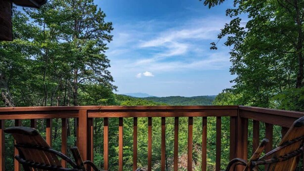 A wooden deck with four Adirondack chairs facing a forested landscape. - Cute Studio Cabin! Views! Private. Hot Tub. Relax! (Sevierville)