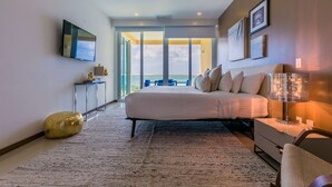 A modern bedroom with a large bed, a TV mounted on the wall, and a view of the outdoors through large windows.
