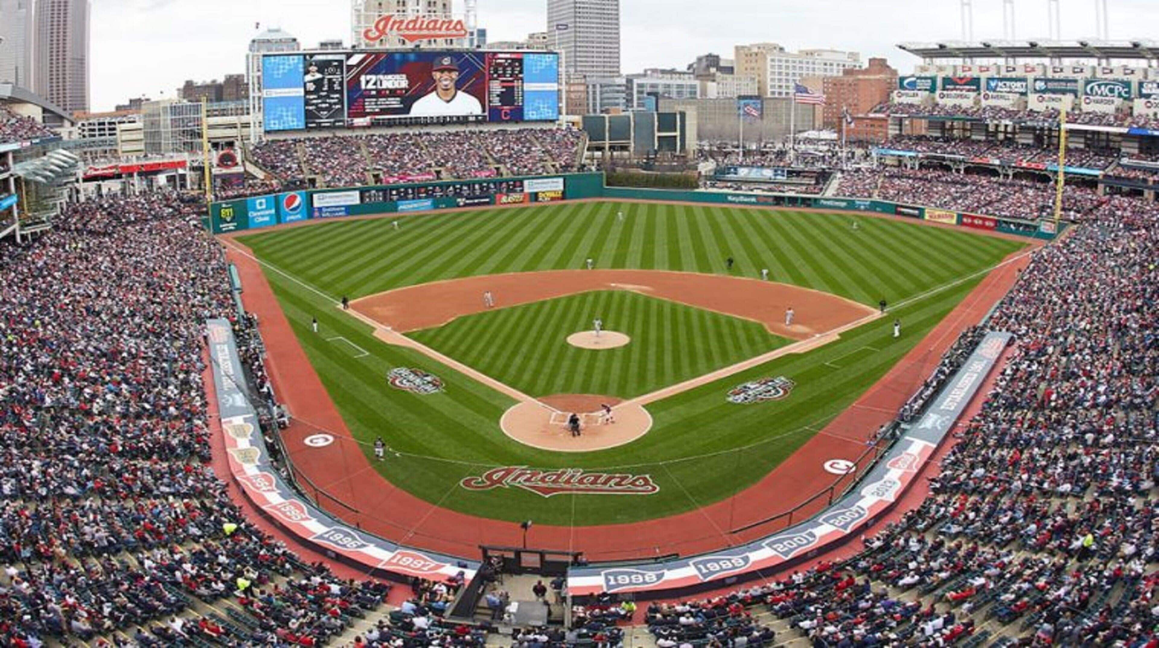 A large stadium with multiple levels of seating, a central field, and a scoreboard.