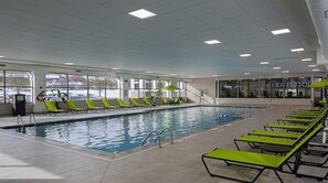 Piscina interior con carriles delimitados, tumbonas y vistas al exterior a través de amplios ventanales.