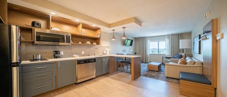 A modern kitchen with built-in appliances, a dining area with a table and chairs, and a living room with a sofa and a TV.