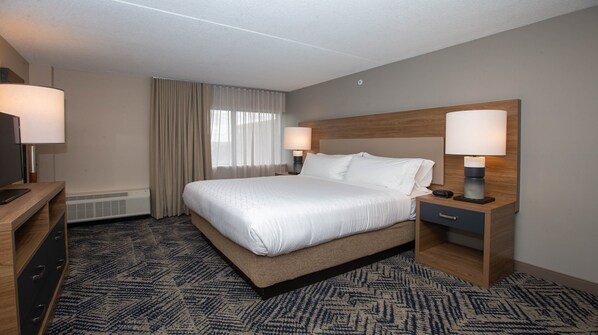 A hotel room with a large bed, two bedside tables with lamps, a desk with a chair, and a patterned carpet.
