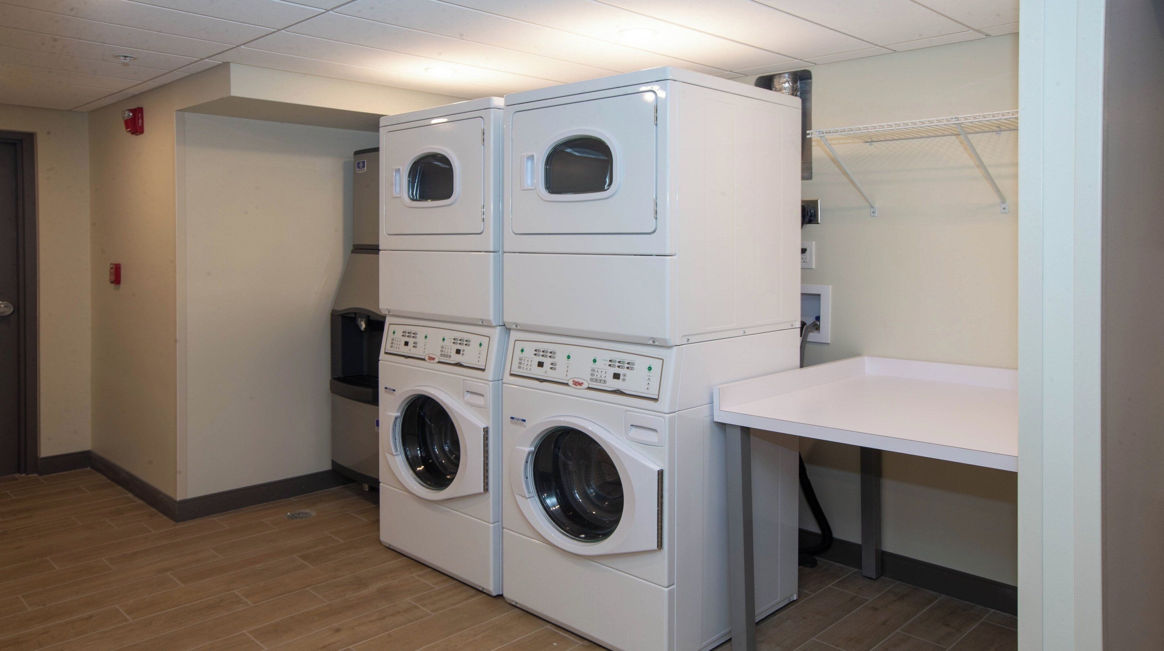 A laundry room with two stacked front-loading washing machines and a table.